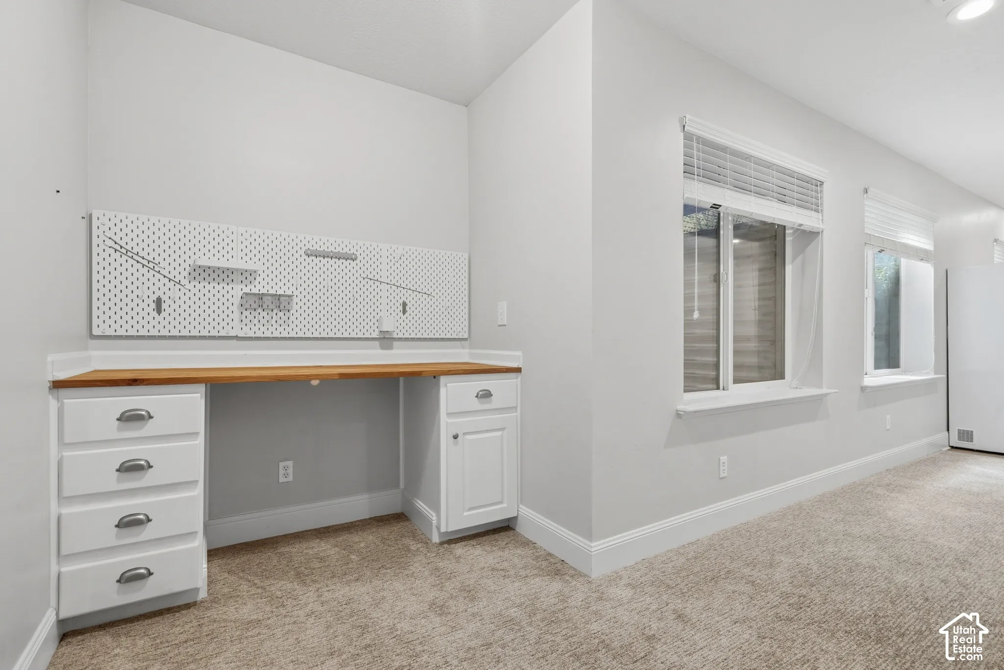 Built-in desk with wood-finish countertop, white cabinetry with silver hardware, and white pegboard