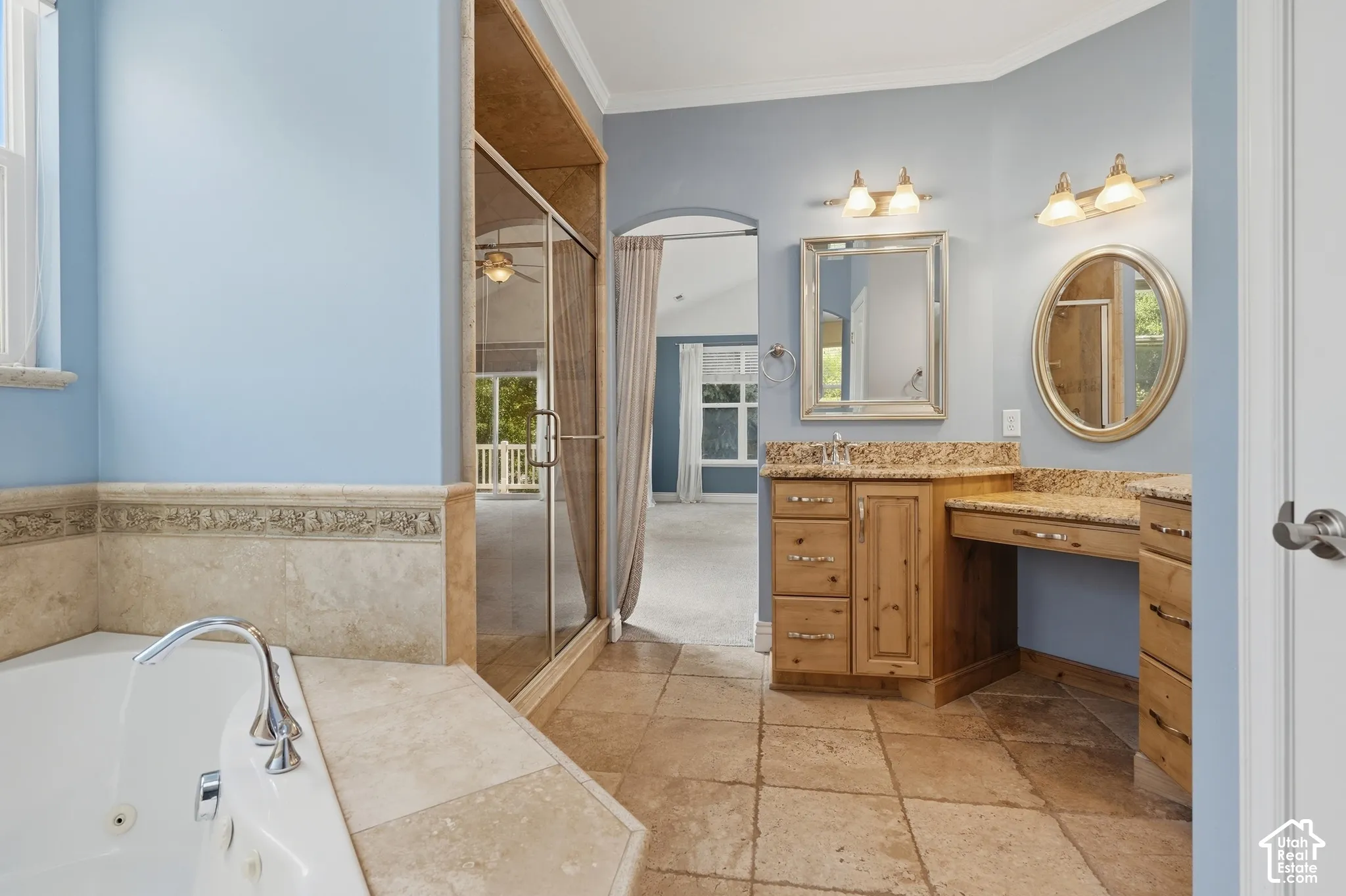 Built-in jetted tub with polished chrome fixtures, glass-enclosed shower, wood-finish vanity with countertop, and tile flooring