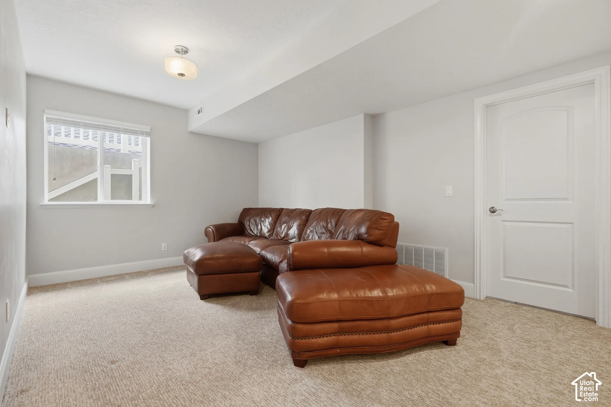 Warm neutral carpeting and light gray walls create a versatile space, complemented by a white interior door with a paneled design