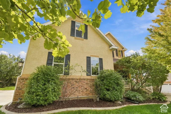 Stucco exterior with brick detailing, featuring multiple windows with black shutters, and mature landscaping