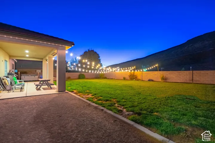 Expansive backyard featuring a covered patio, concrete hardscaping, and a block fence