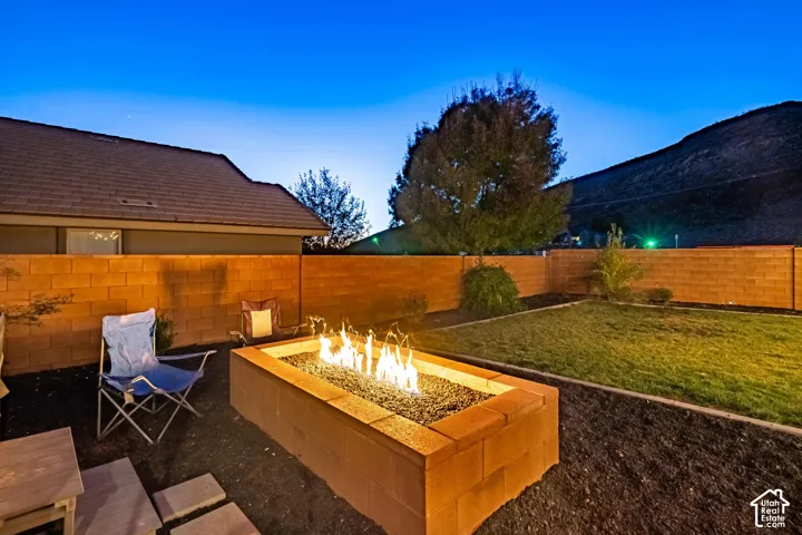 Backyard featuring a built-in fire pit with a stone block surround, gravel, and a manicured lawn