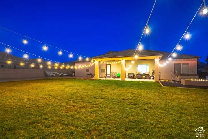 Expansive backyard featuring a covered patio, string lighting, and a built-in fire pit