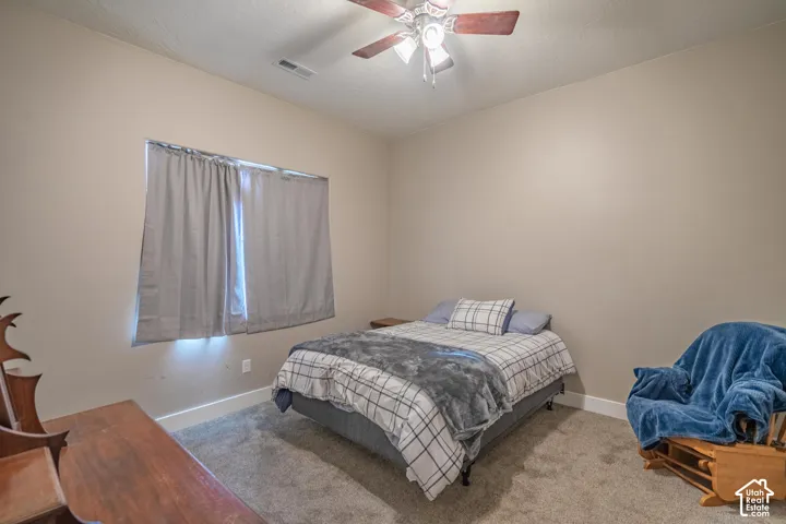 Carpeted flooring, neutral wall tones, ceiling fan with integrated lighting, window with privacy coverings, and white trim