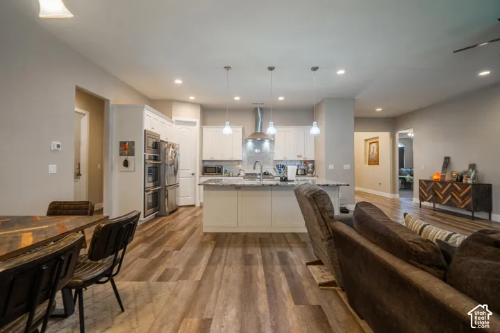 Open concept layout with wood-finish flooring, white kitchen cabinetry, stainless steel appliances, and a kitchen island with pendant lighting