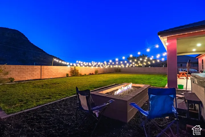 Expansive backyard featuring a manicured lawn, block wall fencing, and a built-in fire pit