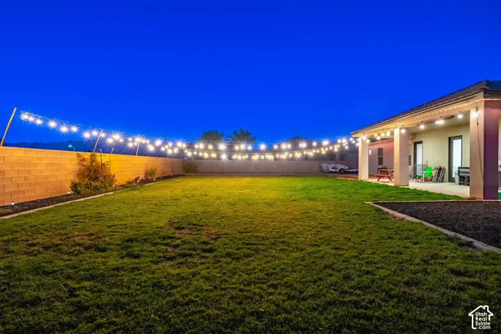 Expansive lawn featuring perimeter string lighting and a block wall