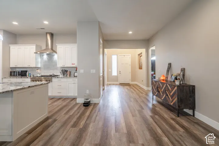 Open concept layout with wood-finish flooring, white kitchen cabinetry, granite-finish countertops, stainless steel range hood, and recessed lighting