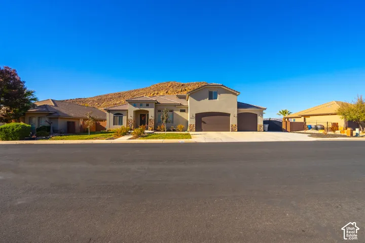 Stucco exterior with stone accents, attached two-car garage, established front landscaping, and a paved driveway