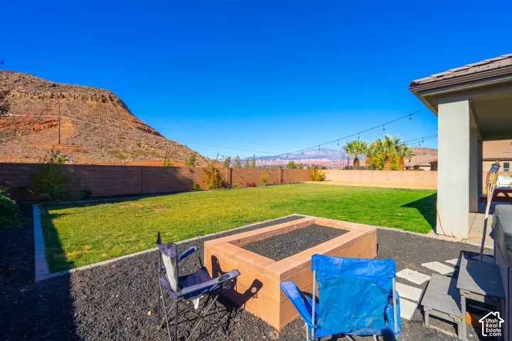 Lush green lawn, built-in fire pit, covered patio, mountain backdrop, and string lighting
