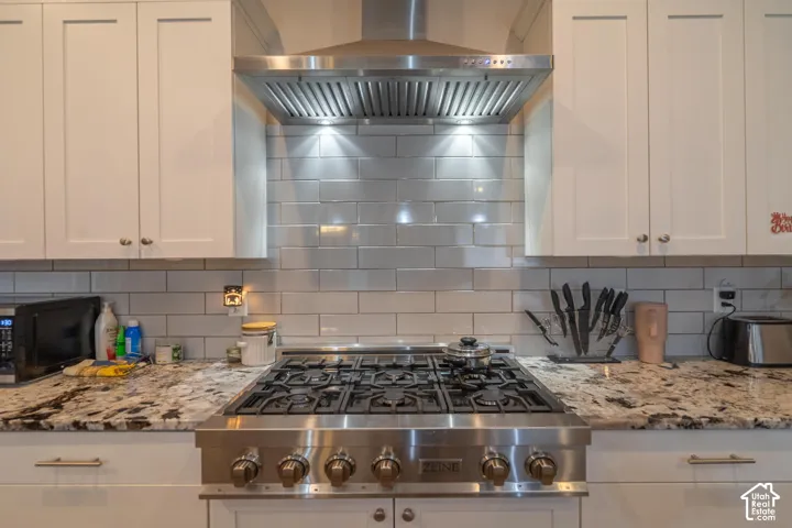 Stainless steel professional-grade range, stainless steel range hood, white shaker-style cabinetry, subway tile backsplash, and granite countertops
