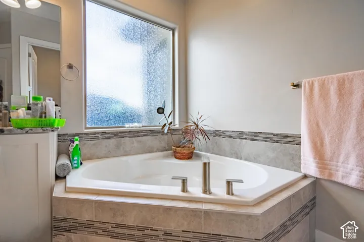 Corner soaking tub with brushed nickel fixtures, tiled surround, and decorative mosaic accent