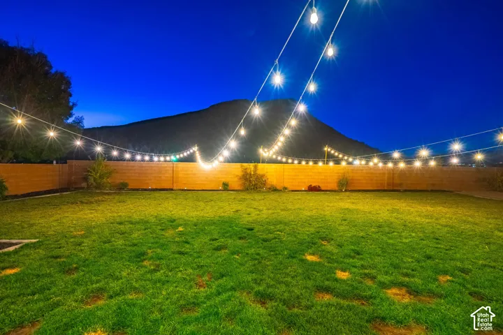 Expansive backyard featuring a manicured lawn, full perimeter fencing, and string lighting
