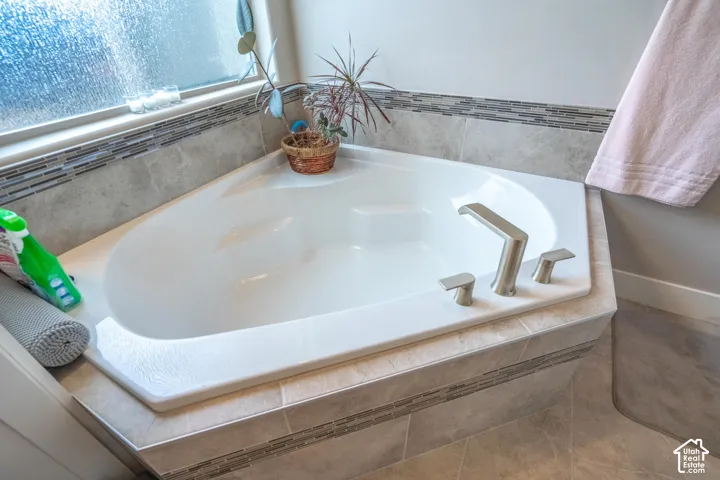 Corner soaking tub with deck-mounted brushed nickel fixtures, tiled surround, and decorative tile accent band
