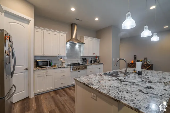 Kitchen featuring white shaker cabinetry, stainless steel appliances, a tile backsplash, wood-finish flooring, and a large island with an integrated sink