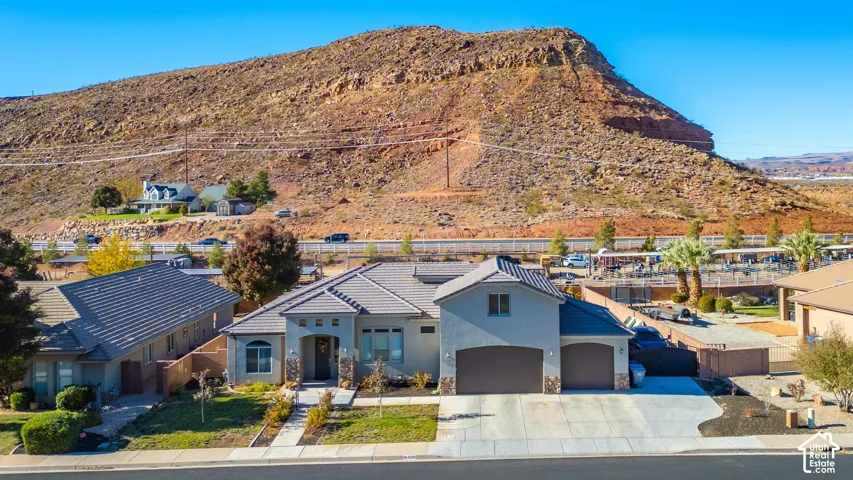 Stucco exterior with stone accents, concrete tile roofing, two-car garage, established front landscaping, and a paved driveway
