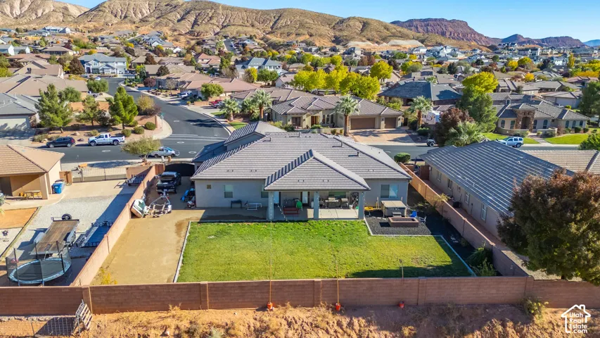 Rear exterior featuring an expansive green lawn, a covered patio, and a dedicated fire pit area