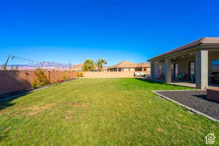 Expansive lawn area with a covered patio, surrounding desert landscaping, and a block fence