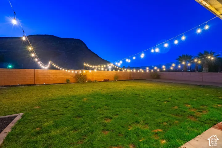 Expansive backyard with a manicured lawn, string lighting, and a block privacy fence