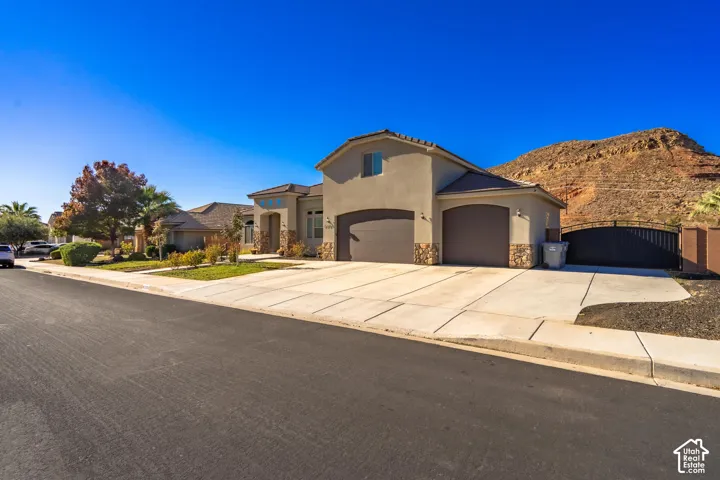 Stucco exterior with stone accents, arched garage doors, a concrete driveway, and a gated side access point