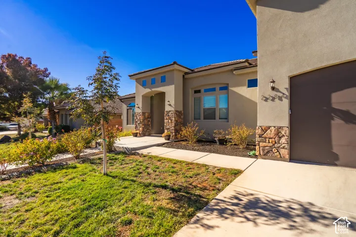 Stucco exterior with stone accents, covered entry, attached garage, and mature landscaping