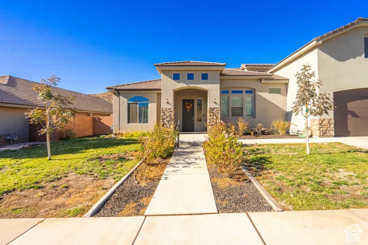 Stucco exterior with stone accents, arched entry, integrated two-car garage, front walkway, and low-maintenance landscaping