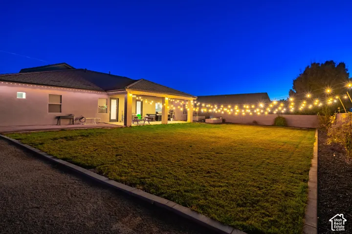Expansive backyard with a manicured lawn, covered patio, string lighting, and a perimeter wall
