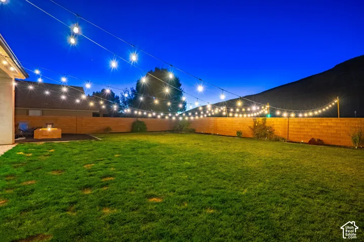 Expansive backyard featuring a manicured lawn, string lighting, and a fire pit