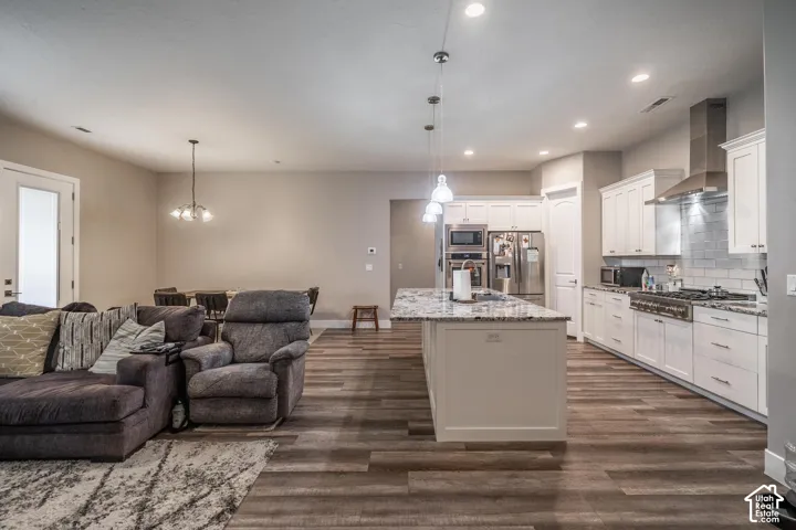 Open-concept living area featuring wood-finish flooring, recessed lighting, a kitchen island with pendant lighting, white cabinetry, and stainless steel appliances