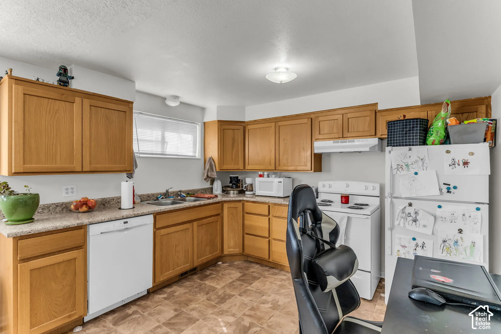 Kitchen featuring wood-finish cabinetry, light-colored countertops, a double basin sink, white appliances, and tiled flooring