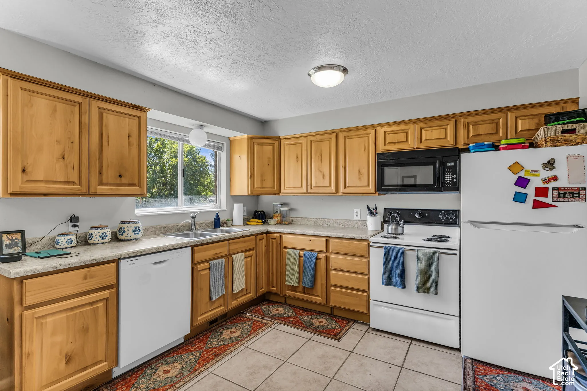 Kitchen featuring wood cabinetry, stone-finish countertops, tile flooring, and integrated white appliances