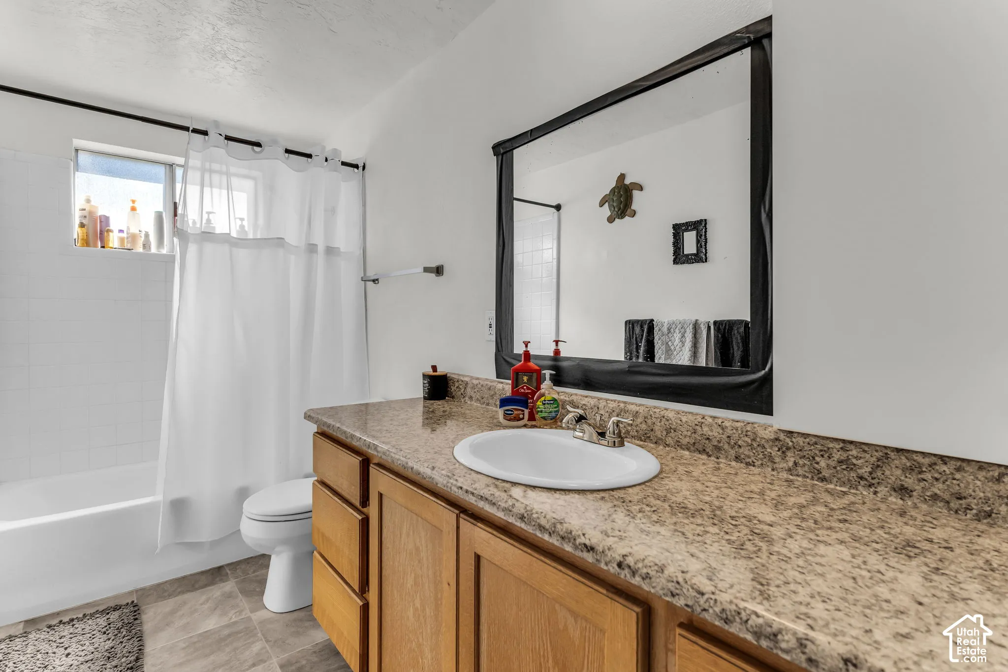 Bathroom featuring a wood-finish vanity with a built-in sink, a speckled countertop, a large wall-mounted mirror, and a tub with a shower