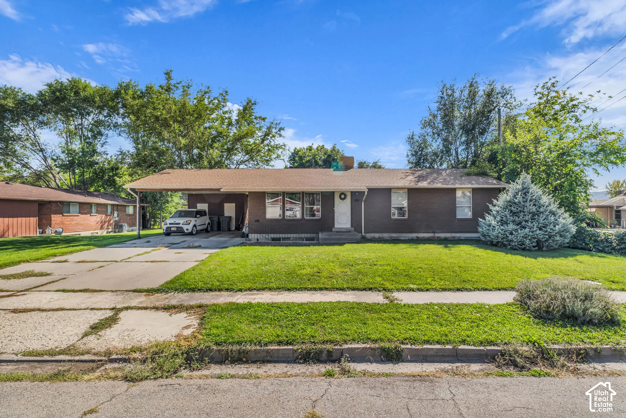 Single-story residence featuring a covered carport, a front lawn, and established trees