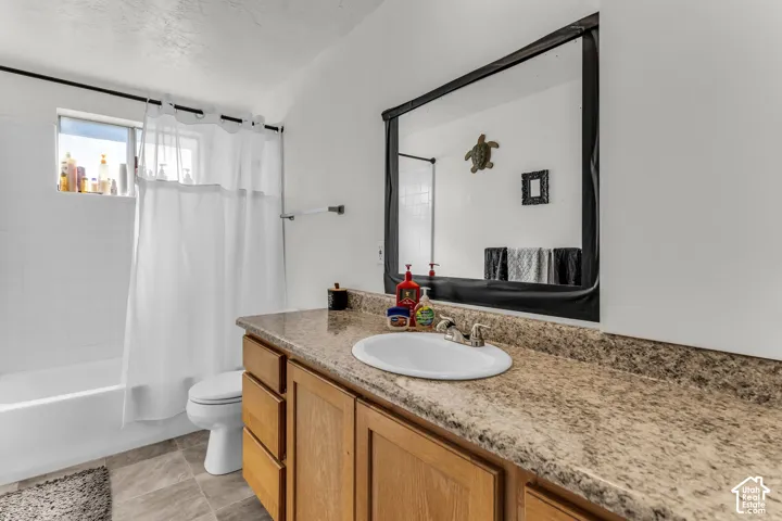 Bathroom featuring a wood-finish vanity with a built-in sink, a speckled countertop, a large wall-mounted mirror, and a tub with a shower
