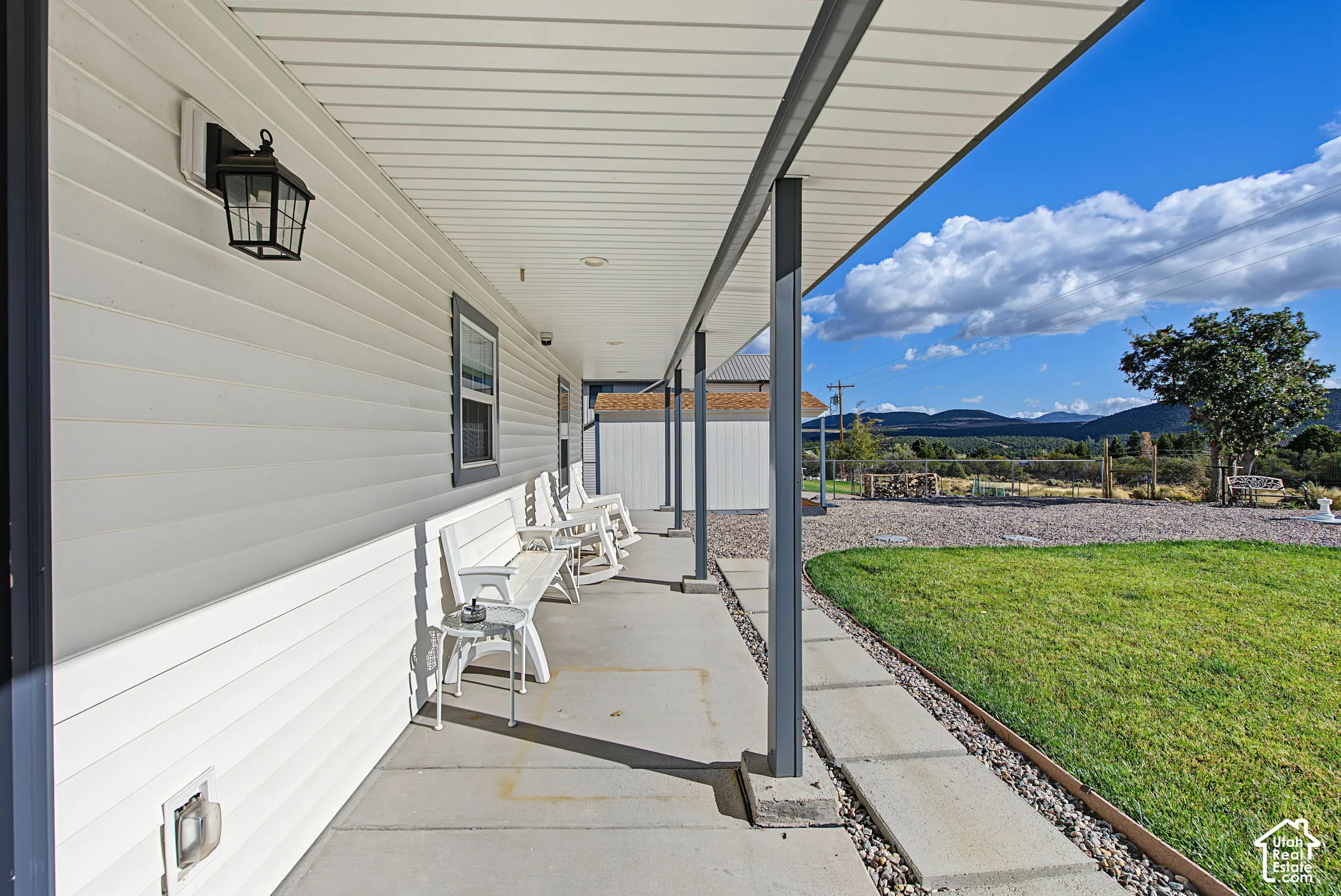 Covered porch with white horizontal siding, dark window trim, and a concrete walkway