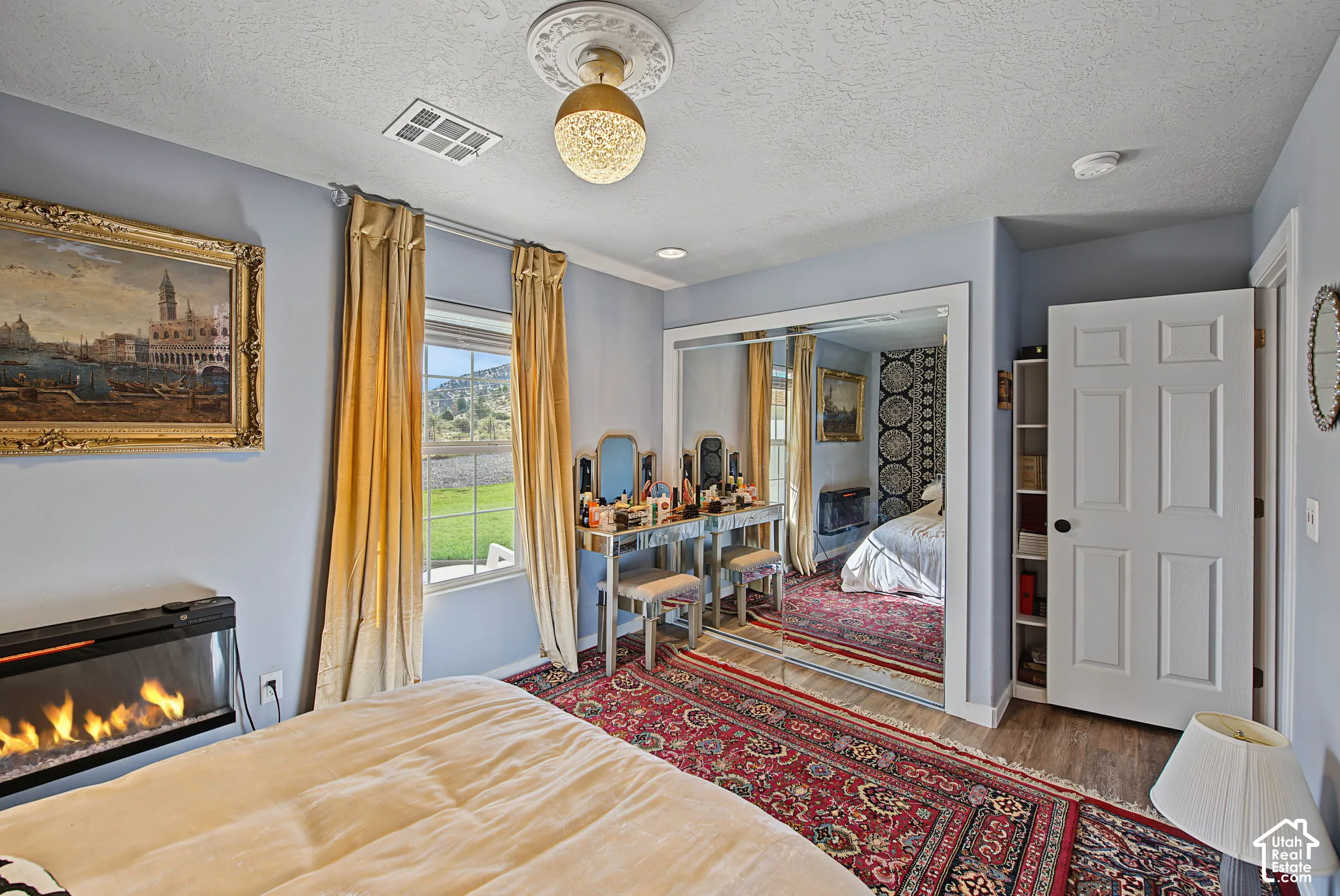 Recessed linear electric fireplace, mirrored closet doors, window with exterior scenery, wood-finish flooring, and a ceiling-mounted light fixture with decorative medallion
