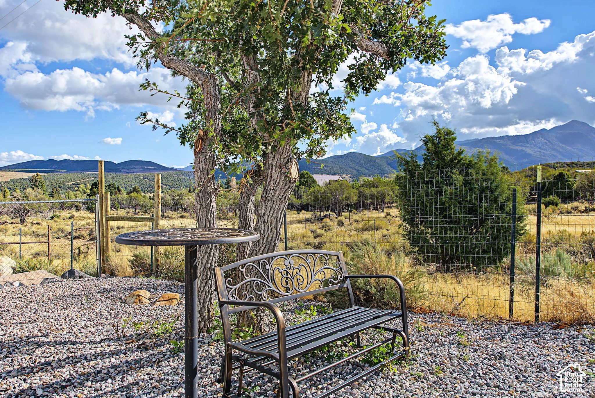 Gravel patio area featuring a mature tree, perimeter fencing, and distant mountains