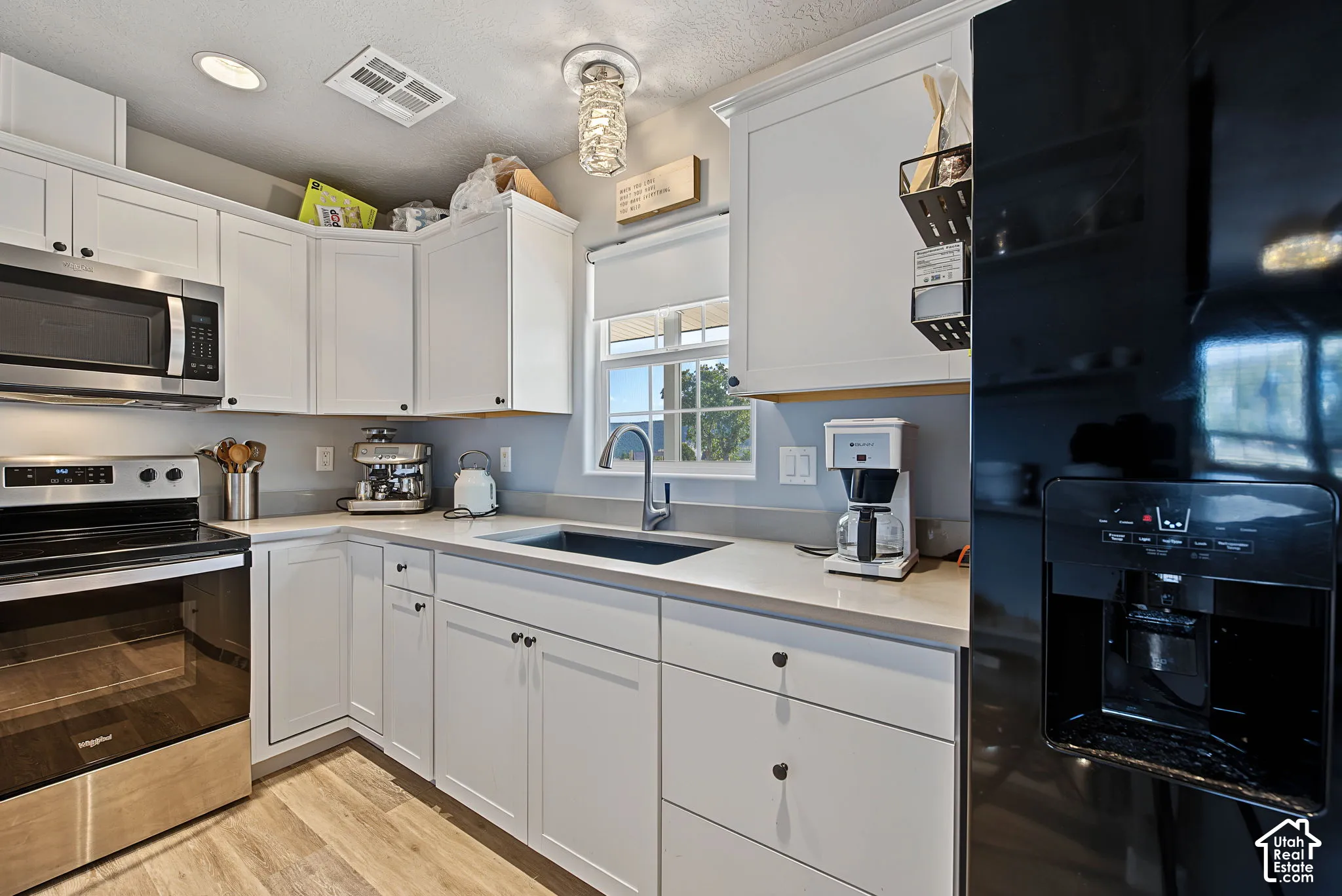 White cabinetry with dark hardware, stainless steel appliances, solid surface countertops, a single basin sink with a gooseneck faucet, and wood-finish flooring