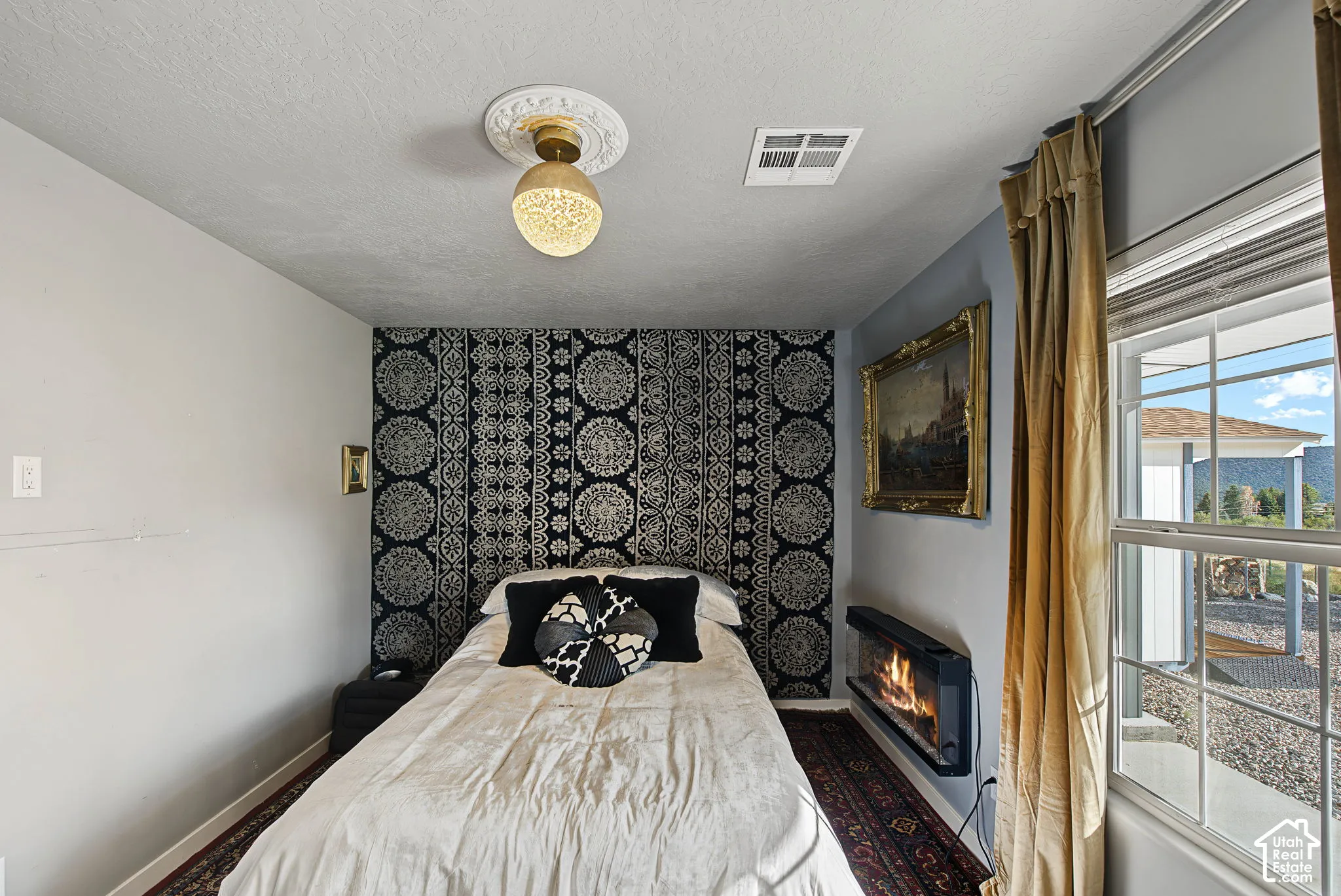 Window with exterior scenery, wall-mounted electric fireplace, ceiling-mounted light fixture, and textured ceiling