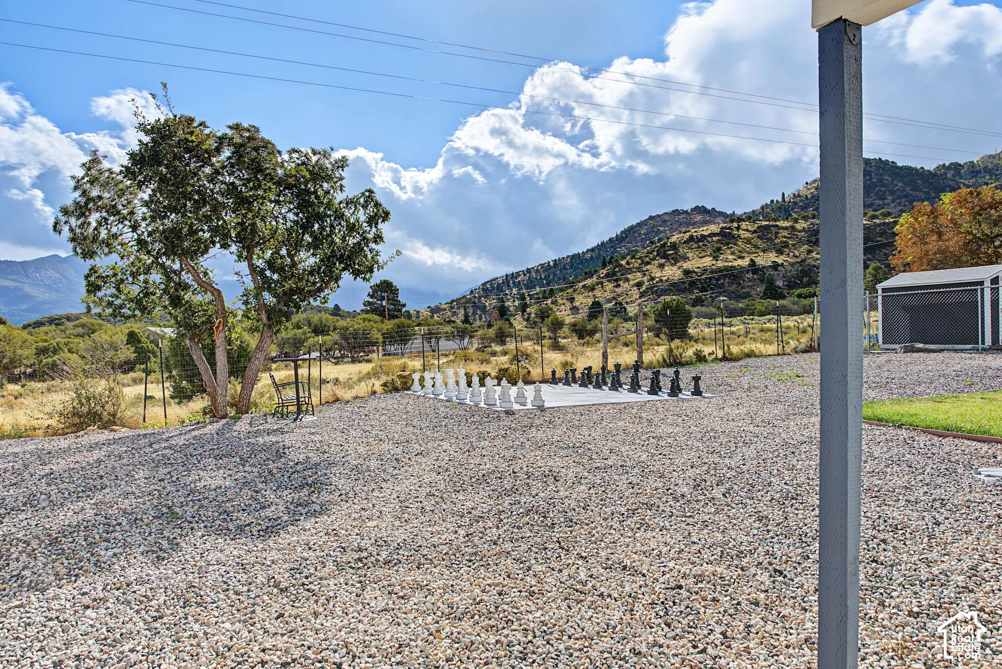 Gravel ground cover with an outdoor chess set and mature tree, set against a mountain backdrop