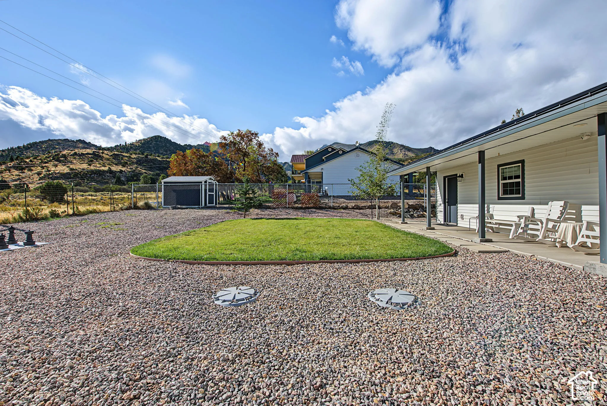 Gravel landscaping with a central grass area, a covered concrete patio, and a detached storage shed