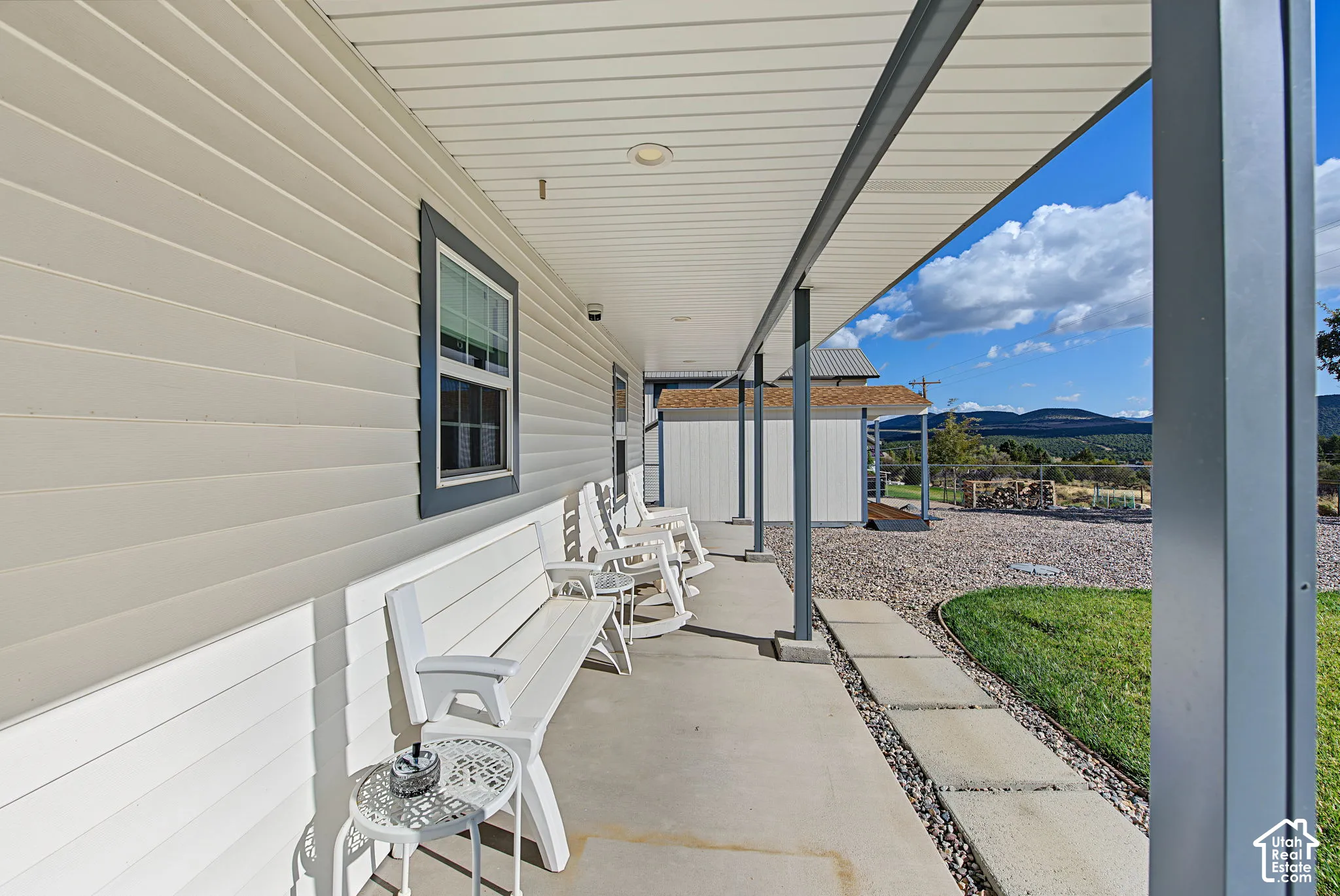 Covered concrete porch with white horizontal siding and dark trim windows