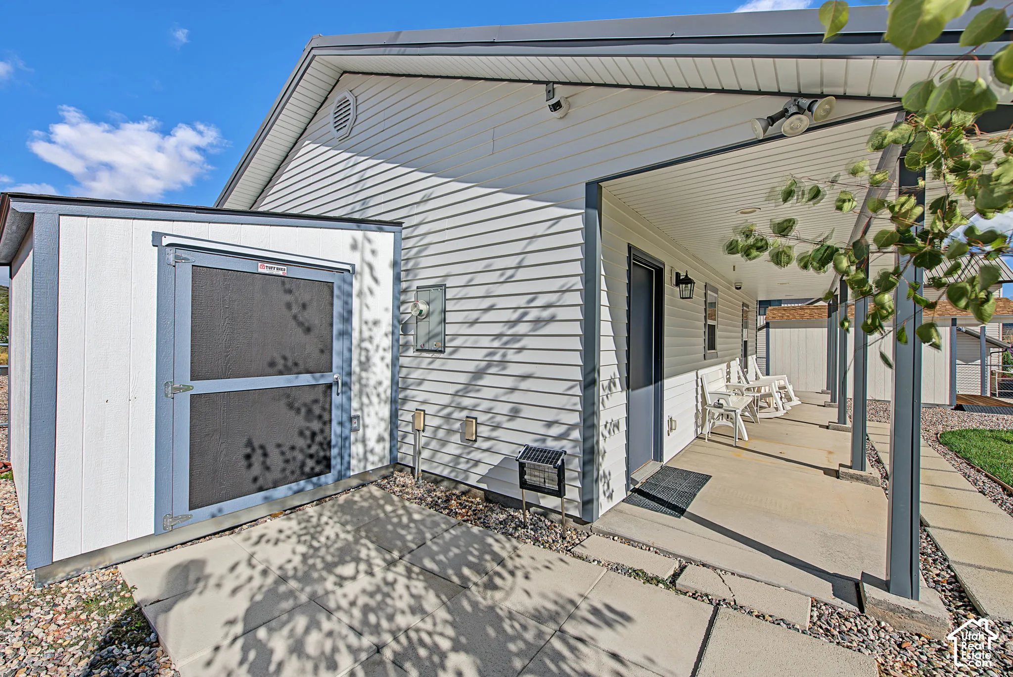 Covered porch with white siding and gray trim, featuring a concrete walkway and gravel landscaping