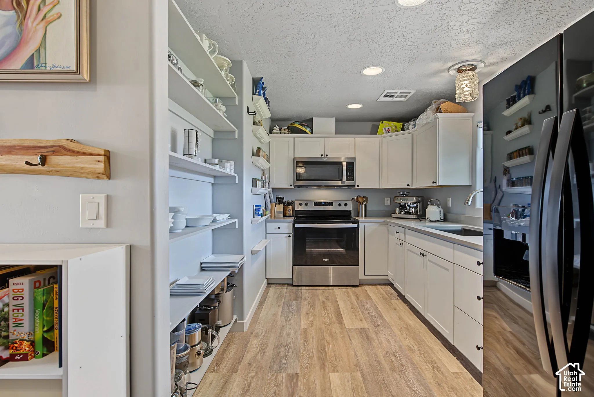 Kitchen featuring light wood-finish flooring, white cabinetry, stainless steel appliances, and a recessed lighting system