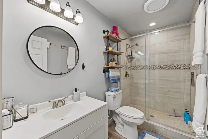 Bathroom featuring a single vanity with a white countertop, a circular framed mirror, a walk-in shower with glass enclosure, and tiled walls