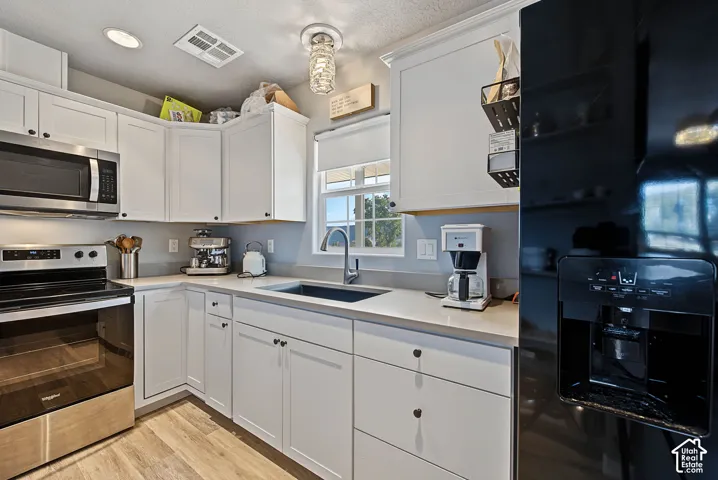White cabinetry with dark hardware, stainless steel appliances, solid surface countertops, a single basin sink with a gooseneck faucet, and wood-finish flooring