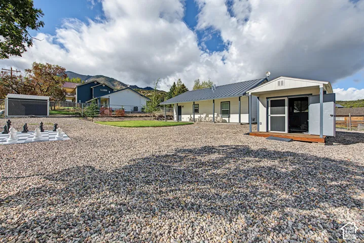 Expansive gravel yard with a dedicated lawn area, featuring a detached shed with a wood-finish porch, and a large outdoor chess set