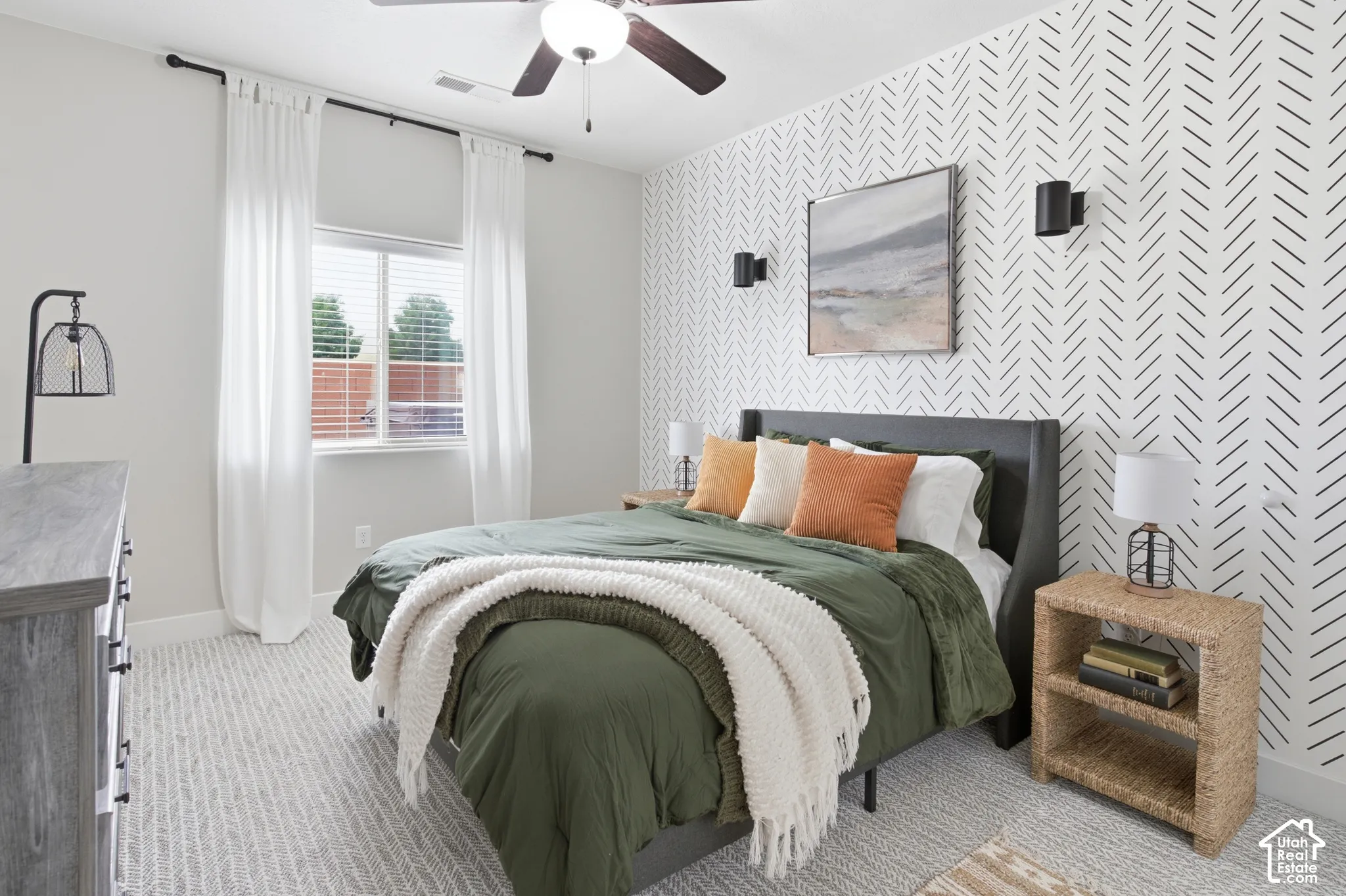Wall-to-wall patterned carpeting, accent wall with a geometric design, ceiling fan with integrated lighting, and a window with blinds