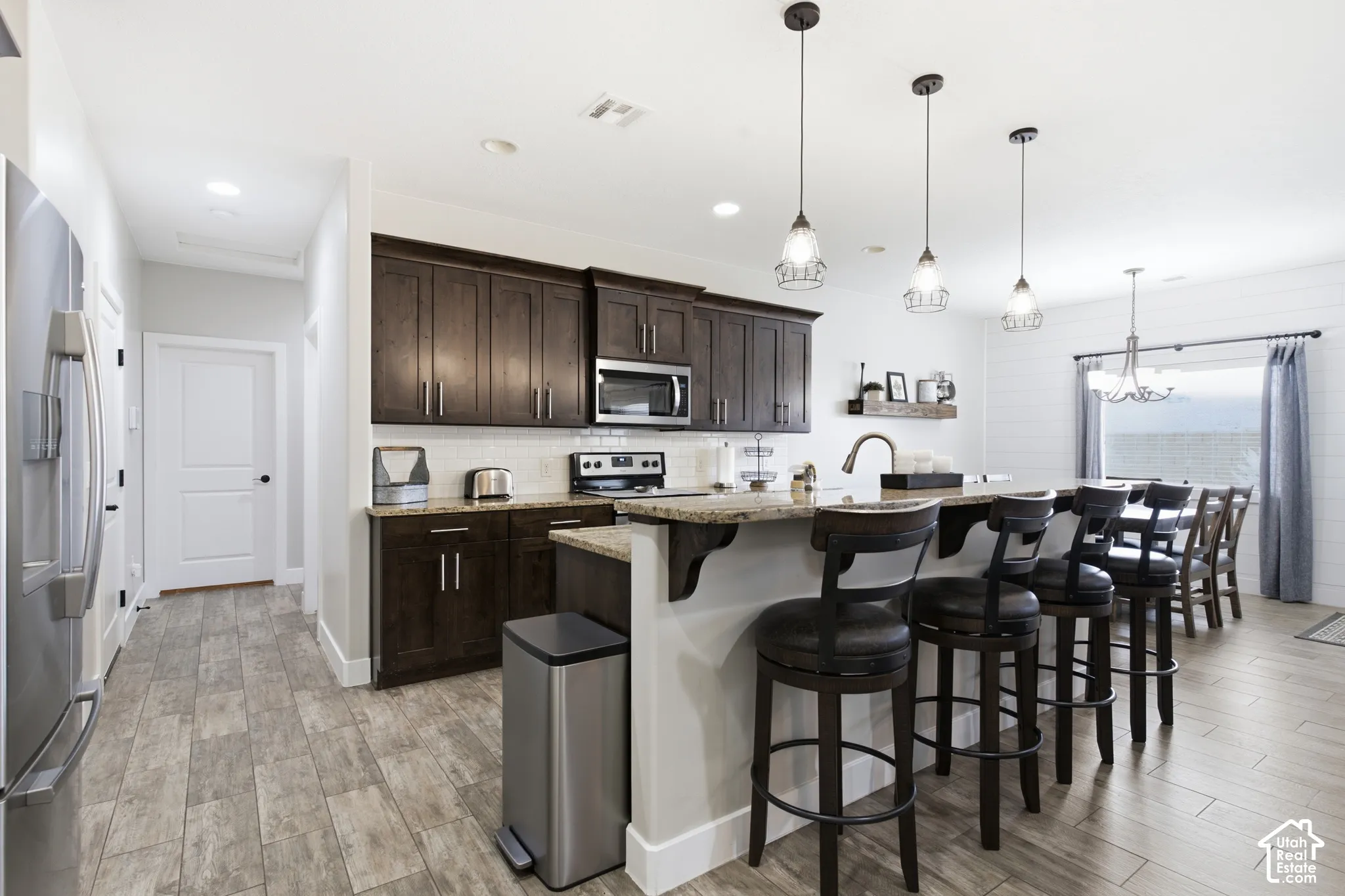 Open-concept kitchen featuring dark wood cabinetry, stainless steel appliances, a center island with bar seating, and wood-finish flooring