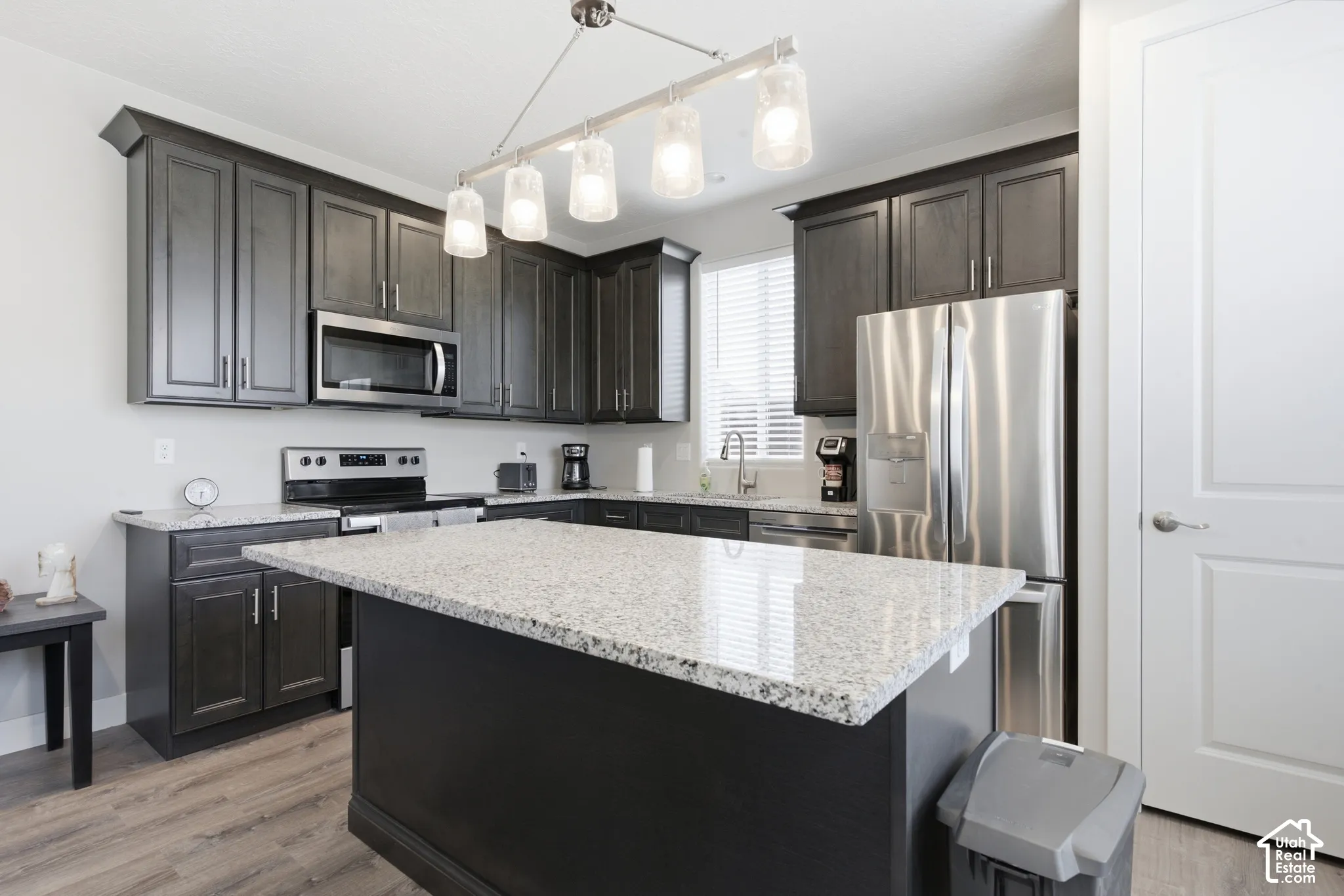 Kitchen featuring dark wood-finish cabinetry, light-colored speckled countertops, stainless steel appliances, a center island, and wood-finish flooring